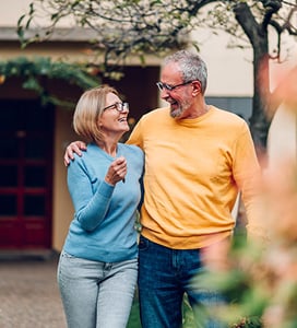 Senior couple embracing each other as they walk outsidew house